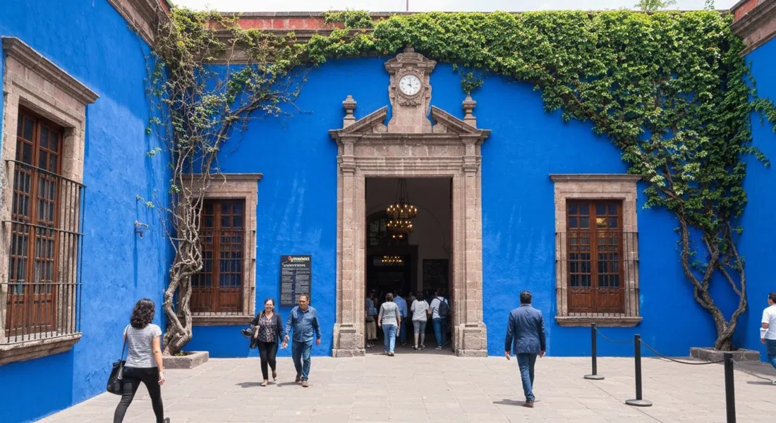 the blue courtyard and leafy entrance at Museo Frida Kahlo, with visitors entering under bright midday sun